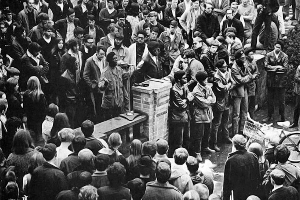 Photo of the Eugene Black Panthers speak on the UO campus in support of a Black student protest at Oregon State University in the late Sixties. From left to right: Oliver Patterson, Tommy Anderson (speaking), Howard Anderson, William Green, Jerome Foster, Julius Hurst, Dennis White, Darrell Fields, Teo DeRuso and Artie Cox.